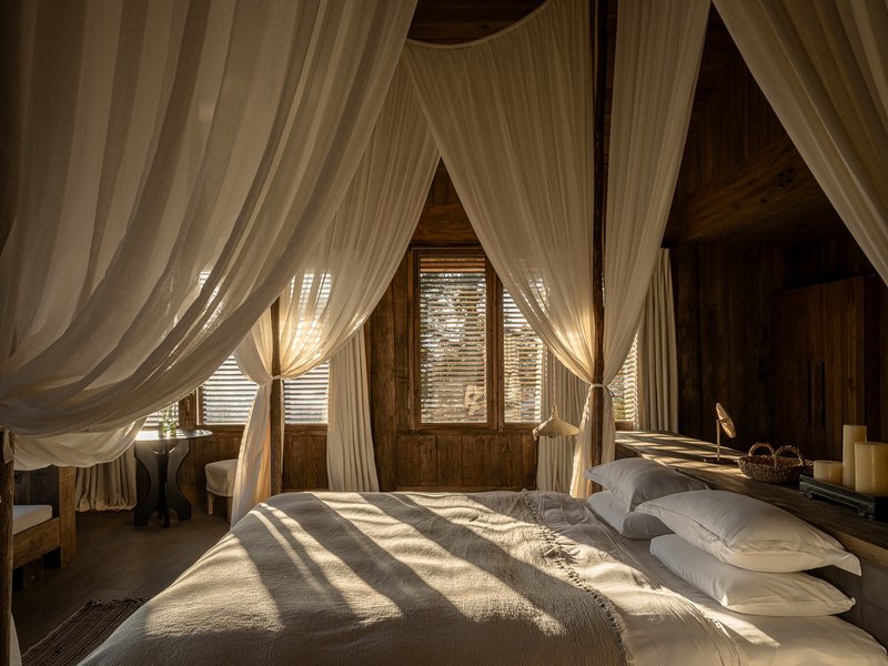 Bedroom with canopy bed draped in sheer curtains and timber louvers filtering sunlight onto the bedding