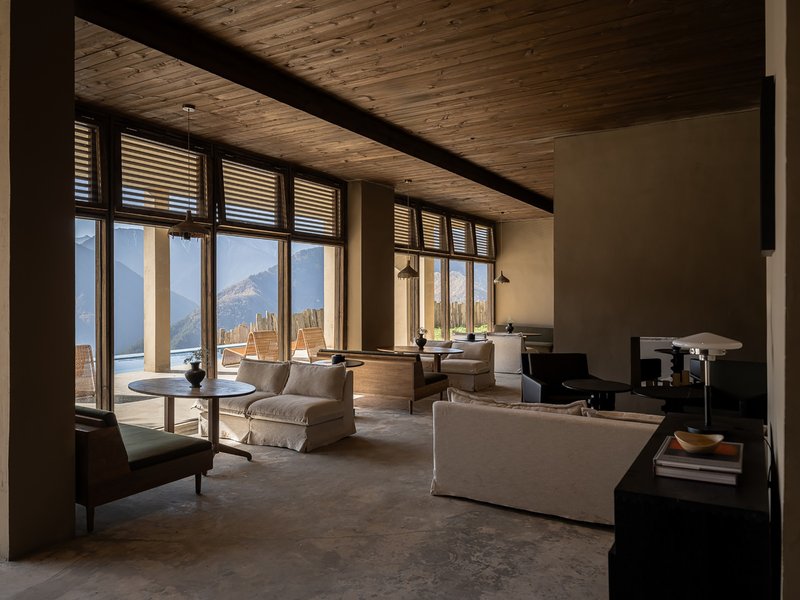 Lounge area with exposed timber beams and row of windows overlooking a terrace and mountain range
