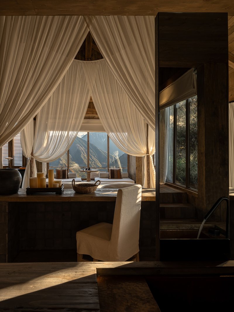Interior with sheer curtains framing triangular window openings and mountain views in afternoon light