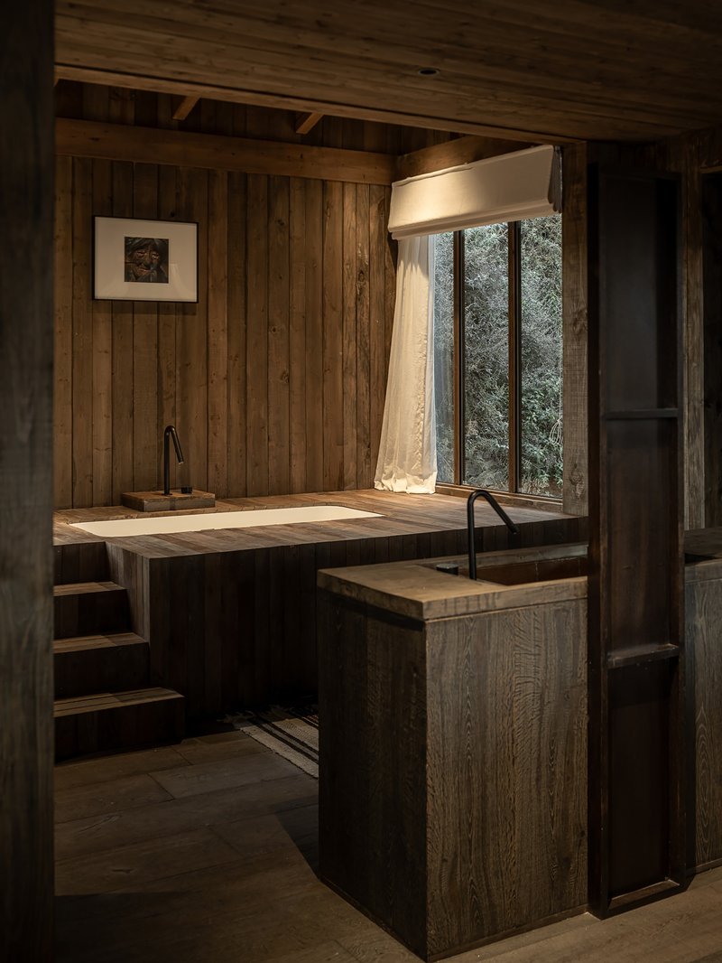 Timber-lined bathing room with sunken tub and tall window framing trees outside