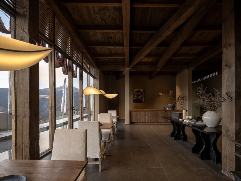 Open-plan interior with exposed timber columns and beams overlooking terraced hillsides through glass walls