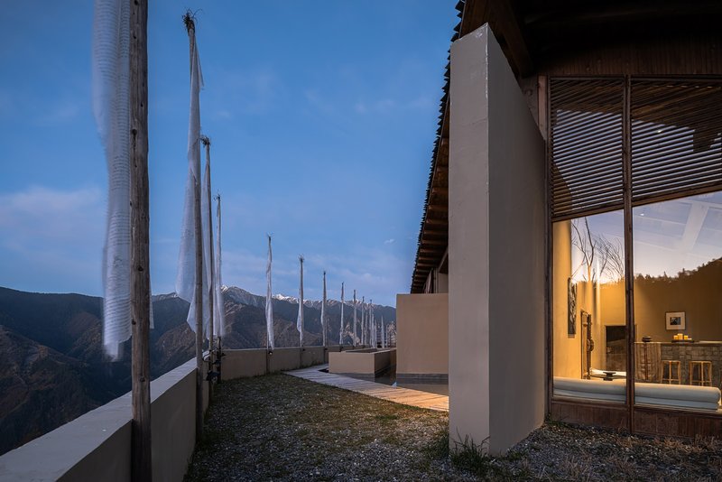 Rooftop terrace with prayer flags and gravel surface at dusk with mountain peaks in distance