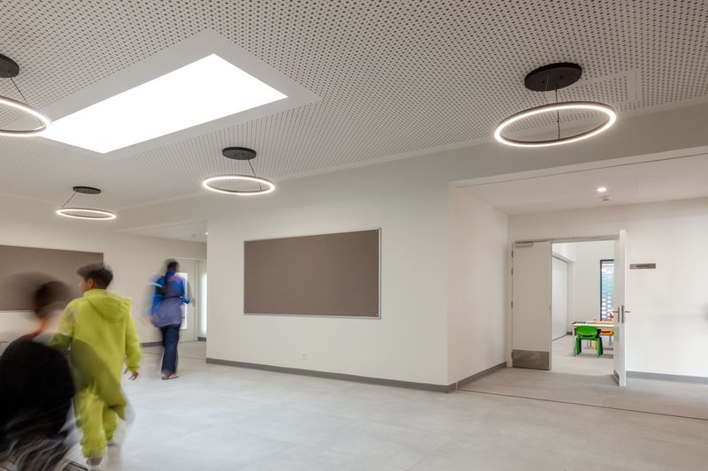 White corridor with circular pendant lights and a skylight casting natural light on people in motion