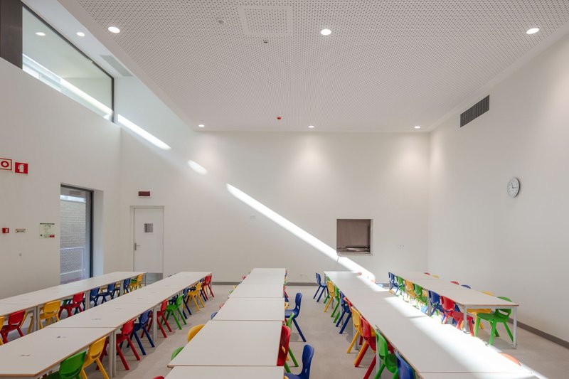 Dining hall with rows of white tables and bright plastic chairs illuminated by clerestory daylight