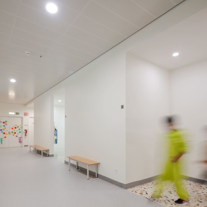 White hallway with terrazzo flooring and timber benches as a person in yellow walks past
