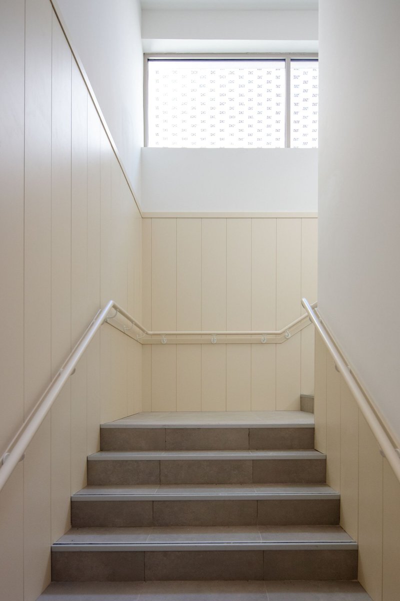 Staircase with pale wood paneling and grey tile treads ascending toward a frosted glass window
