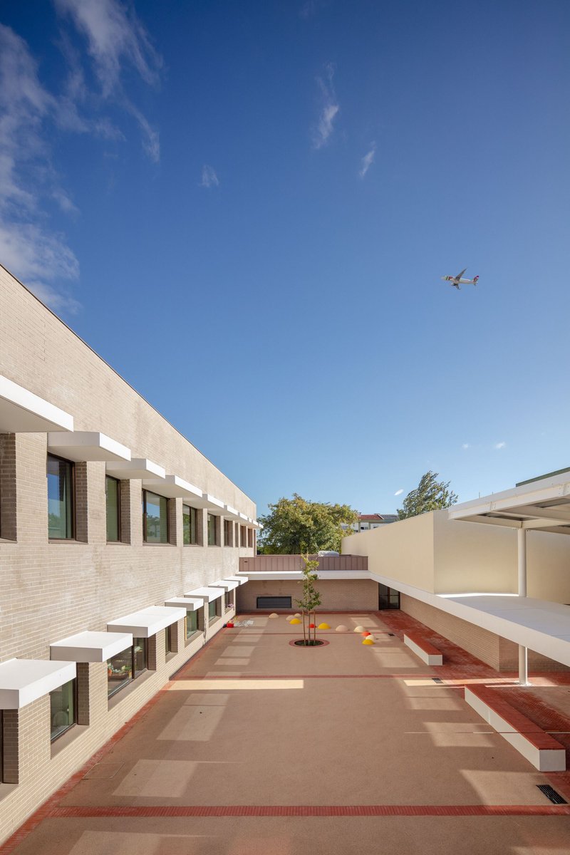 Courtyard with tiled paving in earth tones and red trim beneath a clear blue sky