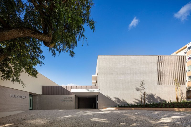 Street view of the library entrance with perforated brick panels framed by overhanging tree branches