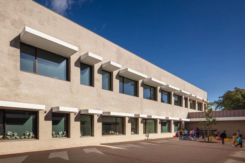 Courtyard facade with repeating canopy shades over glazed openings and children playing below