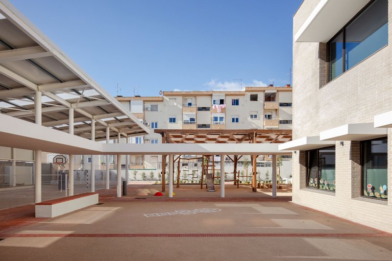 Central courtyard with timber pergola structure connecting volumes around a paved play area