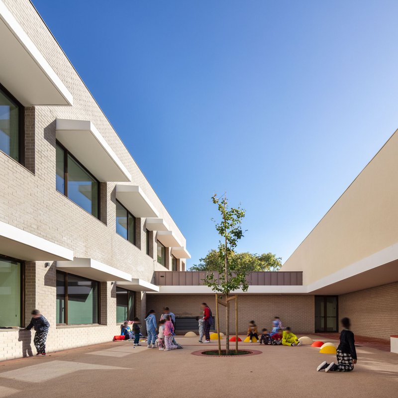 Courtyard view between brick volumes with children gathered around a planted tree bed