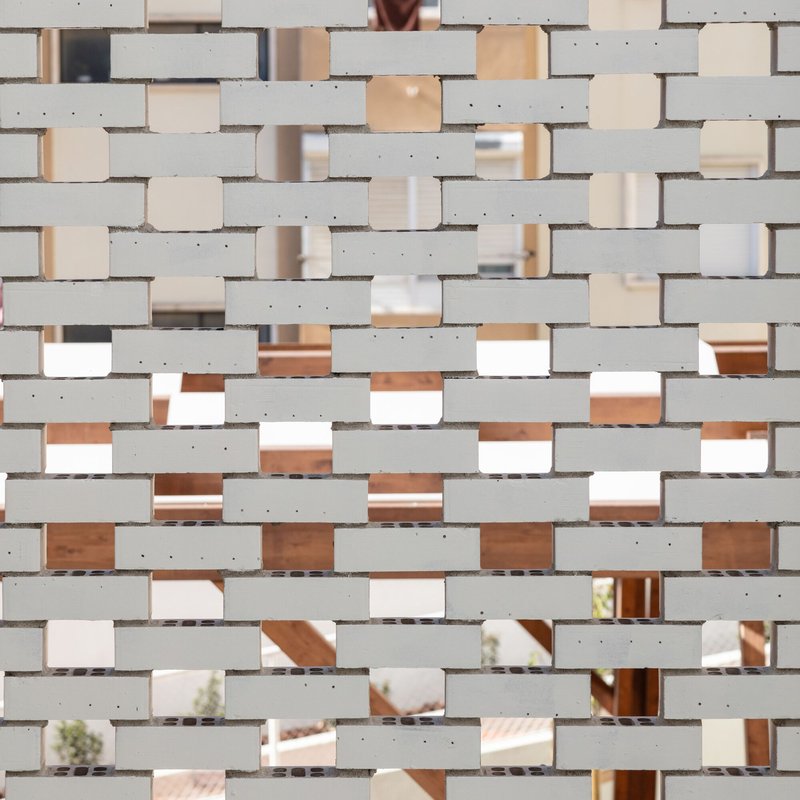 Perforated brick screen with mirrored glass infill creating a patterned translucent facade
