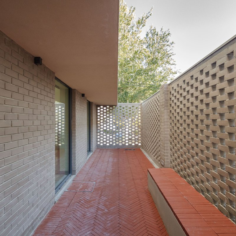 Outdoor terrace with perforated brick screen wall and herringbone tile floor framing tree branches overhead