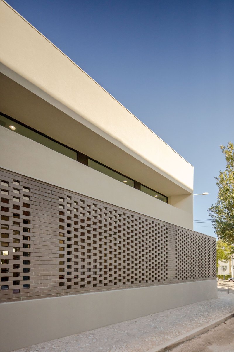Perforated brick screen wall beneath white plaster volume and ribbon window on a clear day