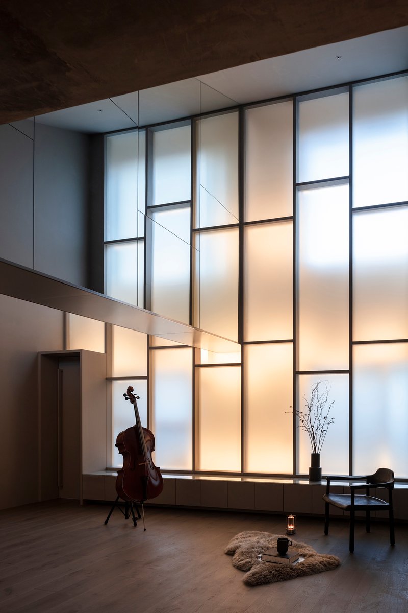 Double-height living space with backlit translucent panel wall and cello in evening light