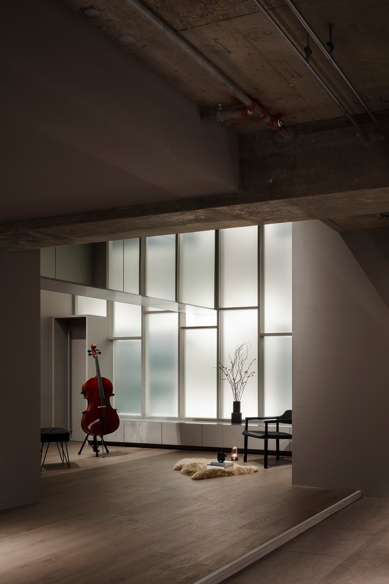 View through exposed concrete beam into space with gridded translucent glass partition and cello on stand