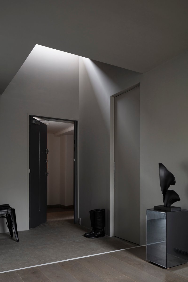 Angled skylight above doorway casting diagonal shadow down pale grey walls and polished floor