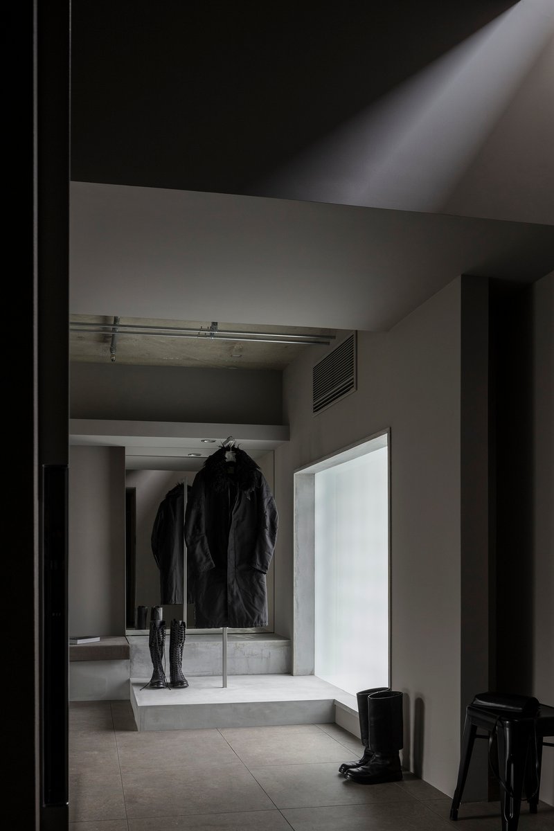 Entry hall with concrete platform displaying coat and boots beneath translucent glass panel