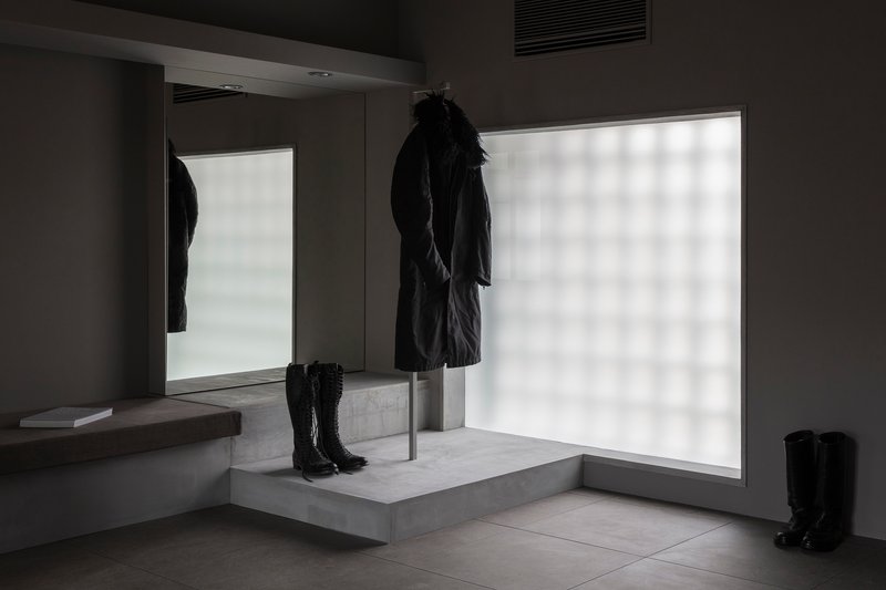 Concrete display pedestal with coat on steel rod and boots against backlit frosted glass