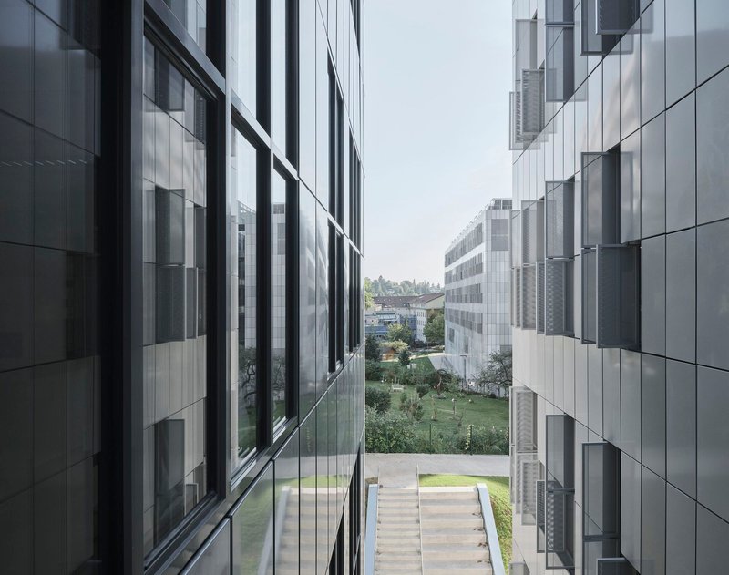View between two aluminum-clad building volumes framing a landscaped courtyard with central stone steps
