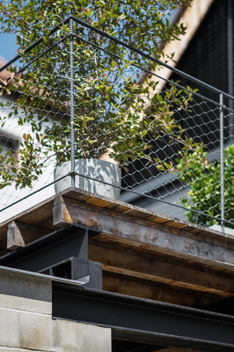 Detail of reclaimed timber beam supporting metal deck with climbing vines on chain-link railing