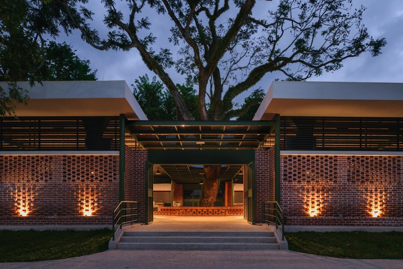 Covered entry portico with timber pergola framing the illuminated brick walls and glass doors at twilight