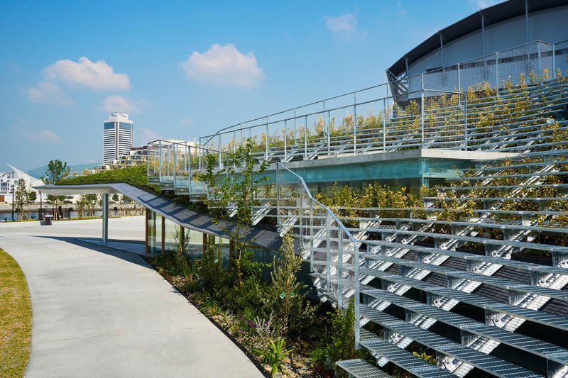 Metal grid terraces with planted rows alongside concrete path and pavilion under partly cloudy sky