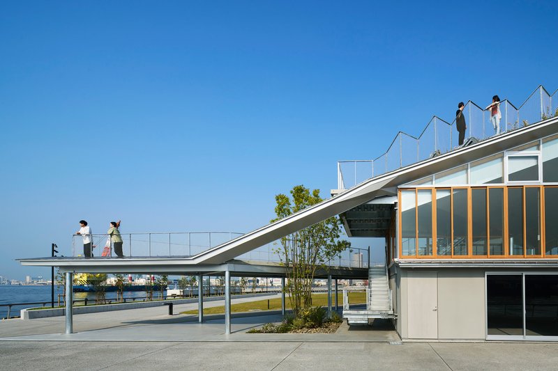 Diagonal roof plane with people standing above glazed facade and waterfront view beyond
