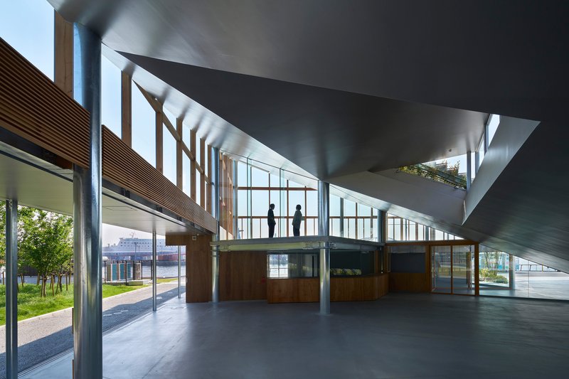 Interior with folded concrete ceiling plane above mezzanine level and timber-clad walls with figures