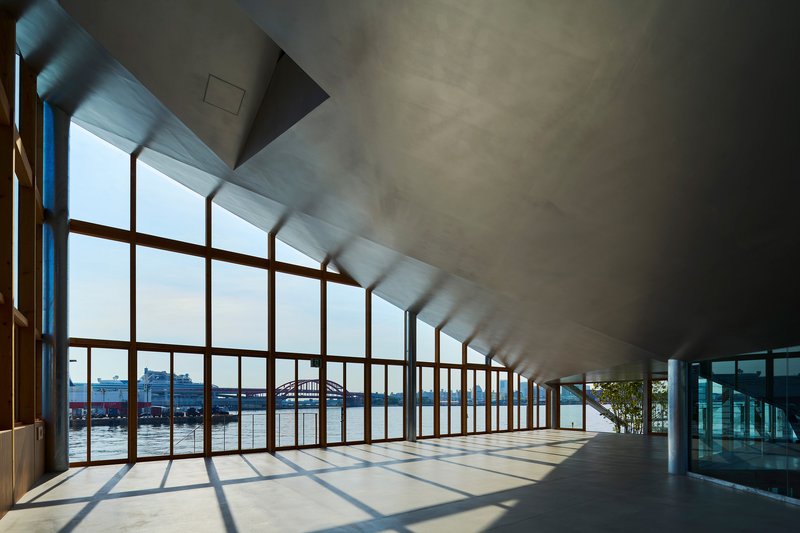 Sunlit corridor with timber curtain wall overlooking water and angled concrete ceiling plane above