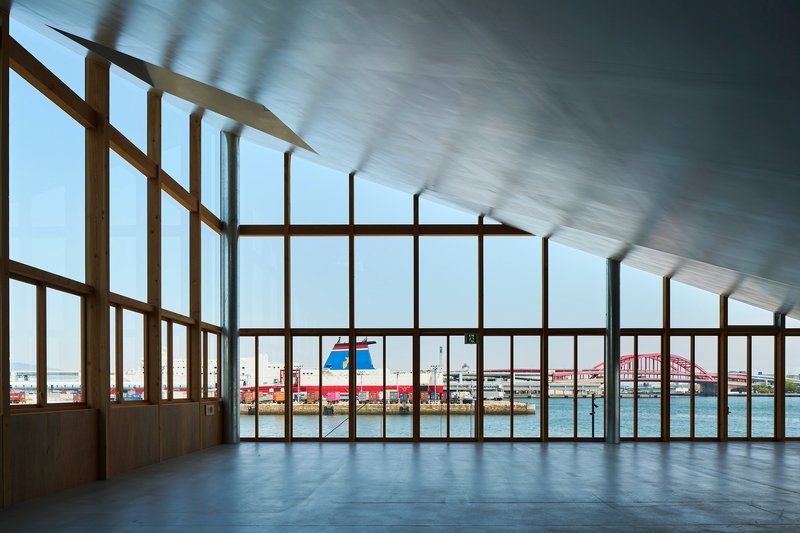 Interior view through timber-framed glazed wall overlooking a harbor with red bridge in the distance