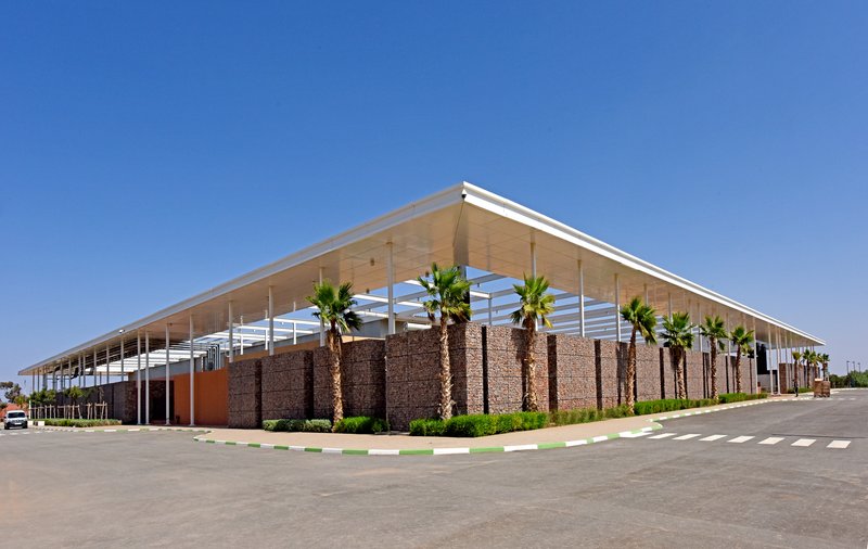 Corner view of the low-slung canopy over gabion walls and palm trees along a paved roadway