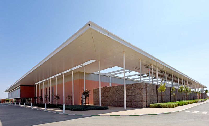 Oblique view of the cantilevered roof with white columns and gabion base under clear skies