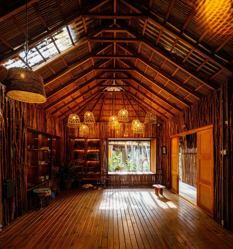 Interior hall with exposed timber trusses, woven pendant lights, and bamboo walls framing garden views