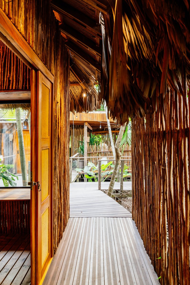 Covered walkway with vertical bamboo screens and palm thatch roof looking toward planted courtyard