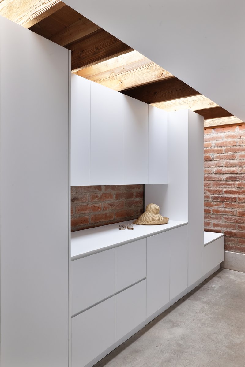 White millwork niche with exposed brick backsplash beneath a staircase with timber soffits