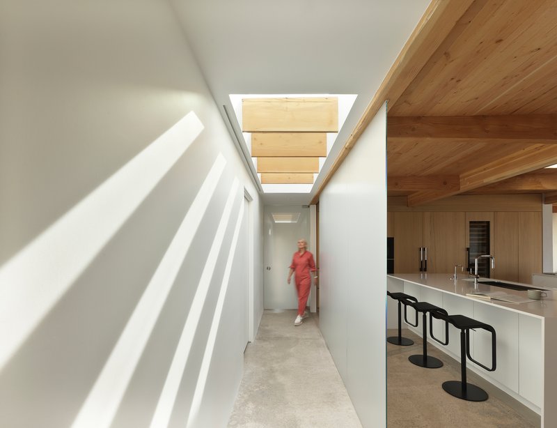 Corridor with overhead skylights casting striped shadows beside a white kitchen counter