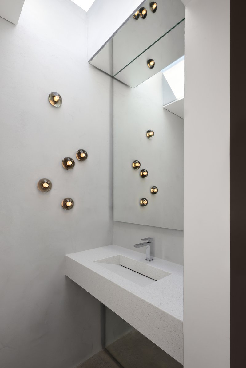 Powder room with white floating vanity, angled mirror, and spherical brass sconces scattered across the wall