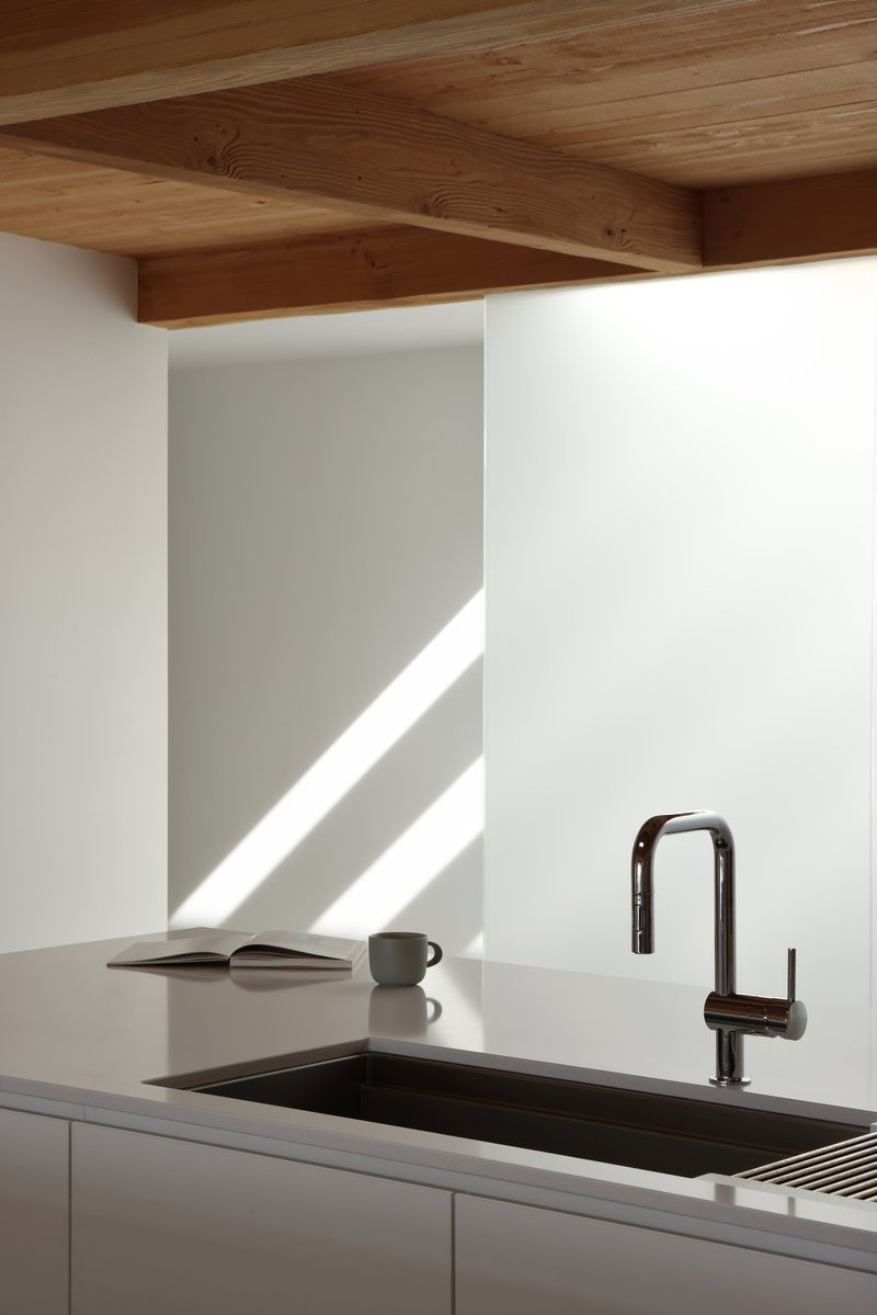 Kitchen counter with black undermount sink and dark faucet beneath timber plank ceiling in morning light
