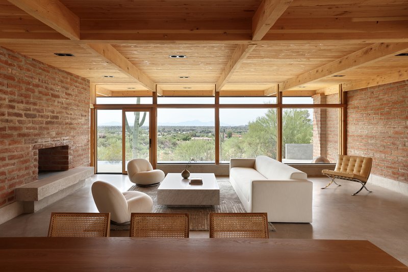 Living room with exposed timber ceiling beams and brick walls framing a panoramic window overlooking desert landscape