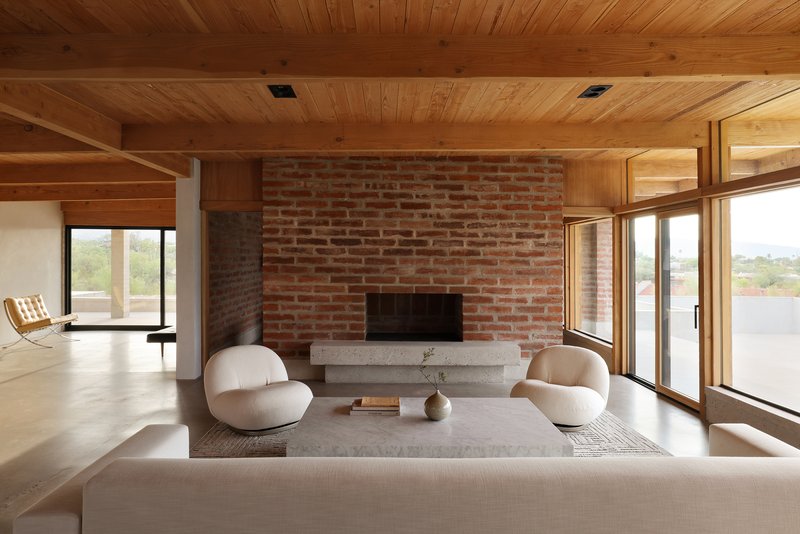 Red brick fireplace wall with concrete hearth beneath a timber plank ceiling with exposed beams