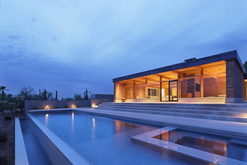 Pool terrace with stepped concrete deck and glazed pavilion with timber ceiling at twilight
