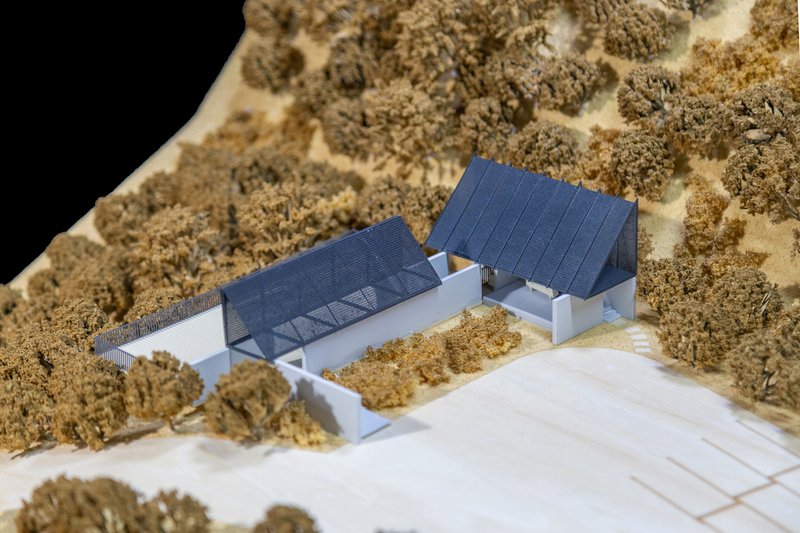 Close-up of physical model showing bridged volumes with corrugated roofs amid foliage