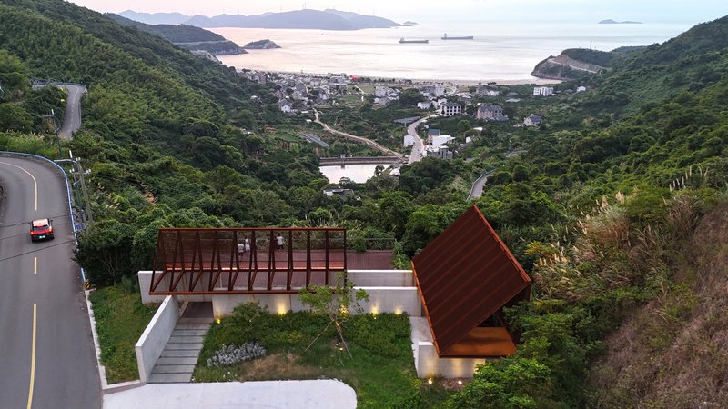 Aerial view of two tilted roof volumes on a hillside overlooking the bay at dusk