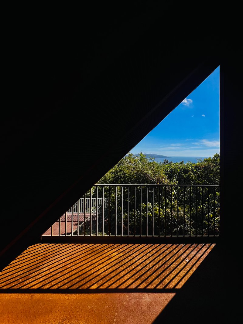 Triangular opening framing a metal railing and ocean view with wooden deck in sunlight