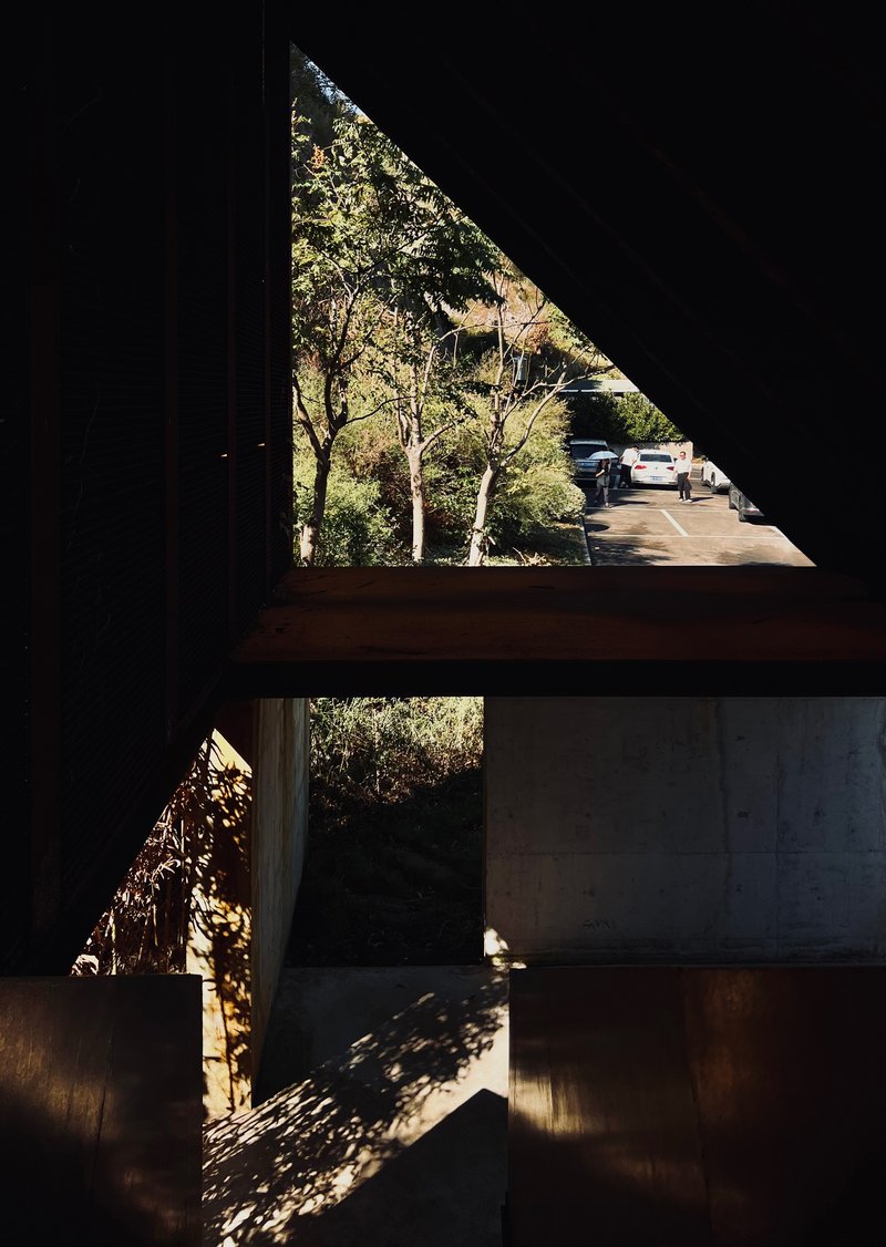 Interior view of triangular window openings with concrete beams casting dappled shadows from trees