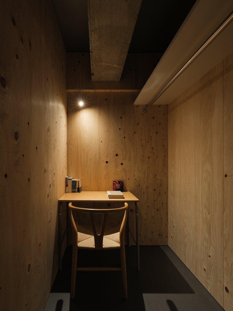 Small plywood-clad study nook with wall-mounted desk and single chair beneath warm overhead lighting