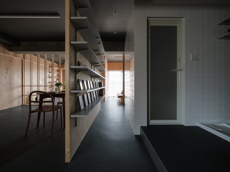 Narrow passageway with grey tile walls and floating steel shelves lined with bottles
