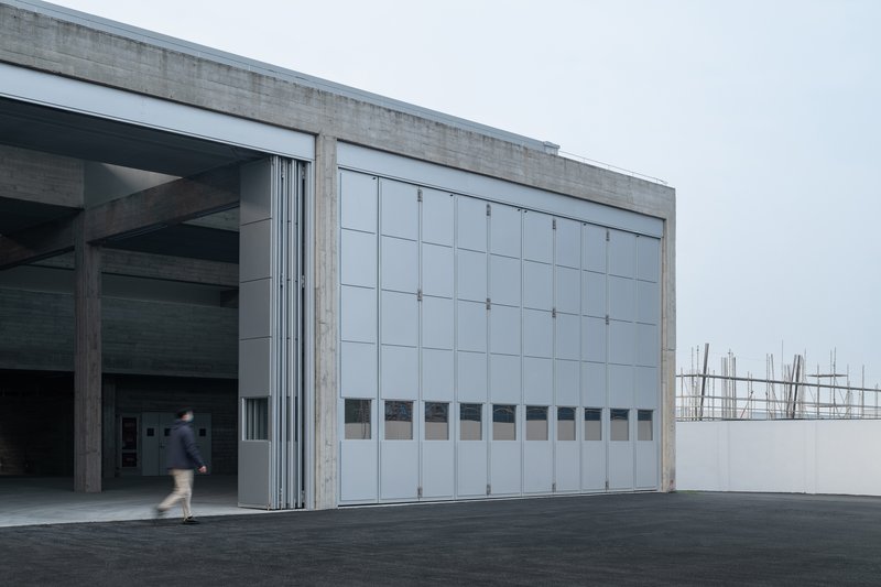Large sliding metal panel doors in concrete frames with a figure crossing the threshold