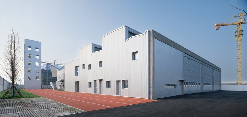 White corrugated metal facade alongside a red running track with construction crane in the distance